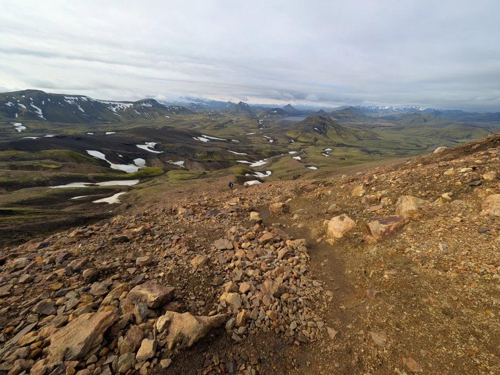 A lone walker on a remote Icelandic slope above a wide volcanic valley